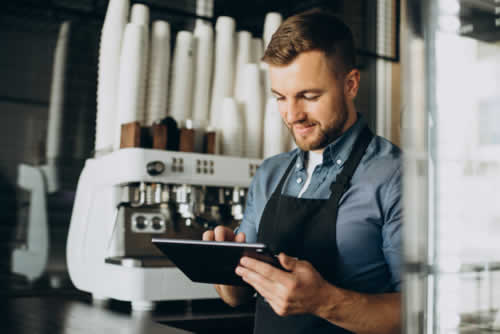 Young man studying using digital tablet behind coffee shop counter
