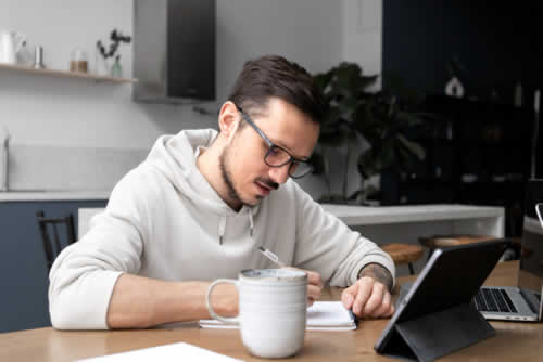 Young man writing notes while working from home desk